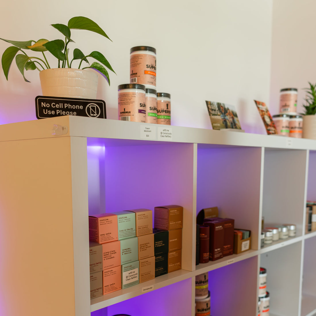 Wellness boutique shelves at Prana Hot Yoga featuring natural skincare, supplements, essential oils, and local artisan products with no cell phone use sign visible