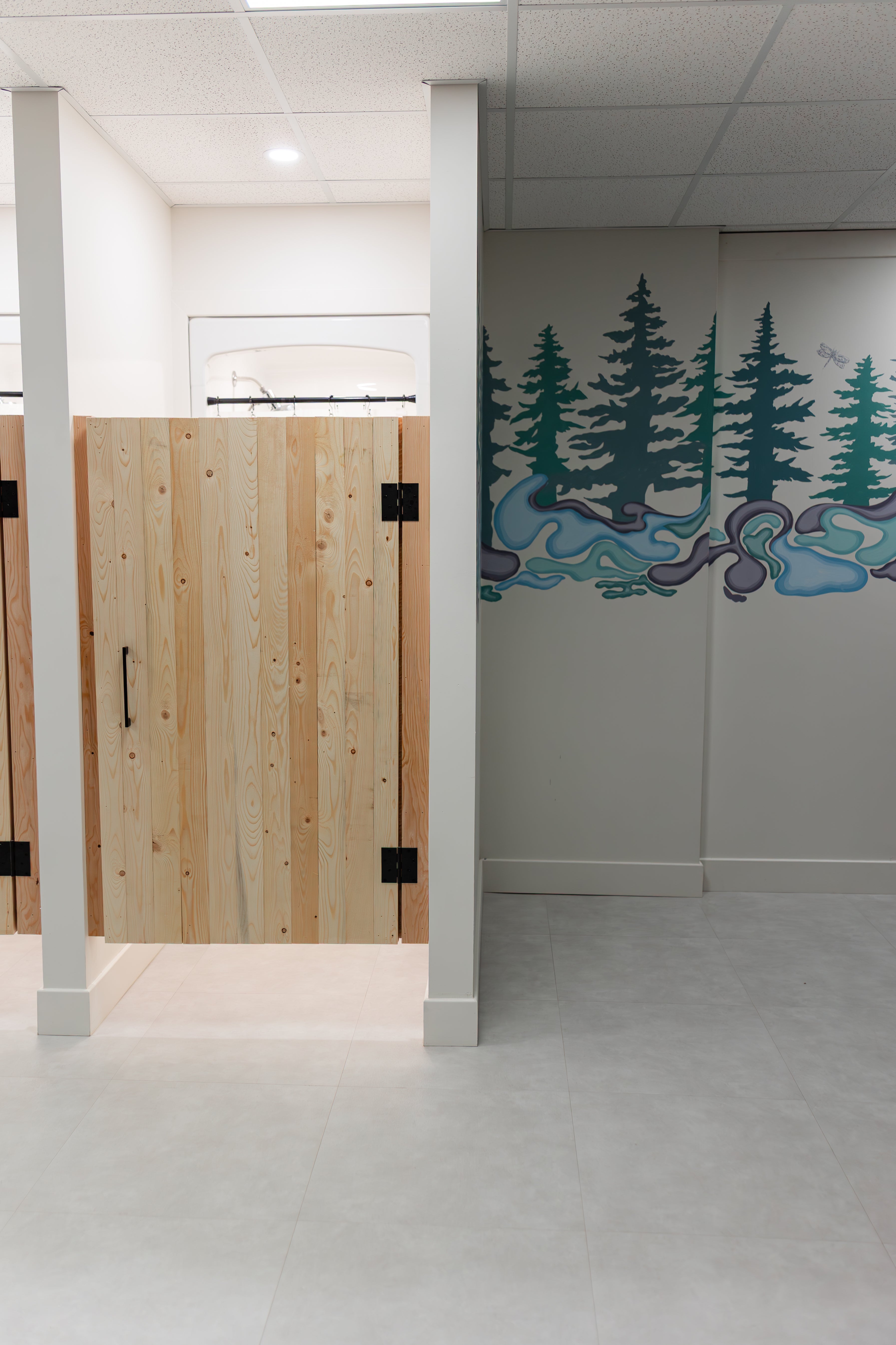 Wood-door shower stalls and a forest wall mural in the Prana Fredericton changing area