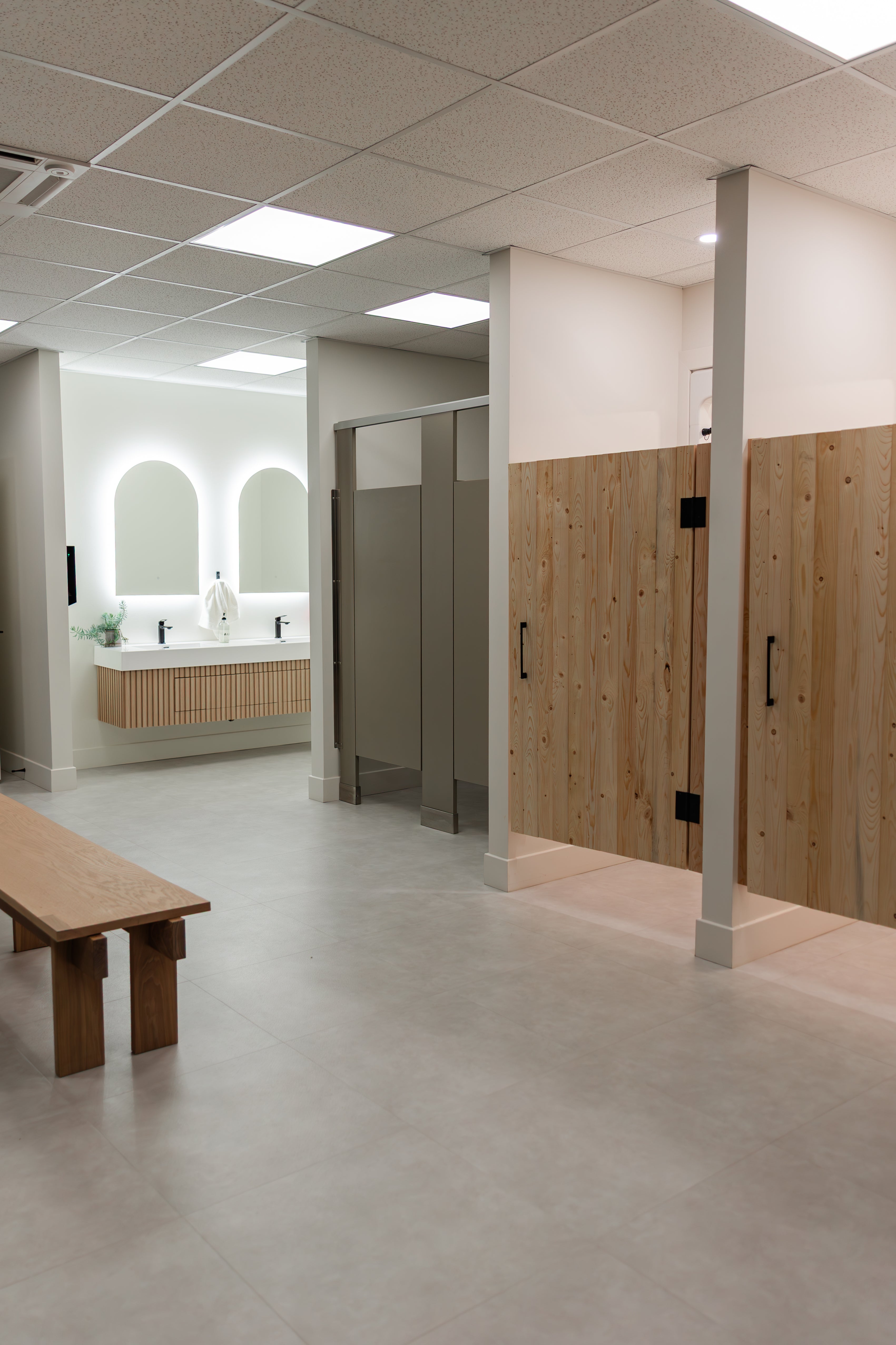 Changing room at Prana Fredericton with shower stalls, restroom stalls, double vanity, and bench