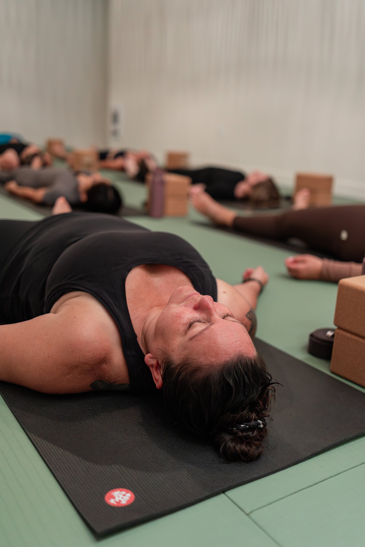 Student resting in savasana after class at Prana Fredericton, with mats and blocks in the studio