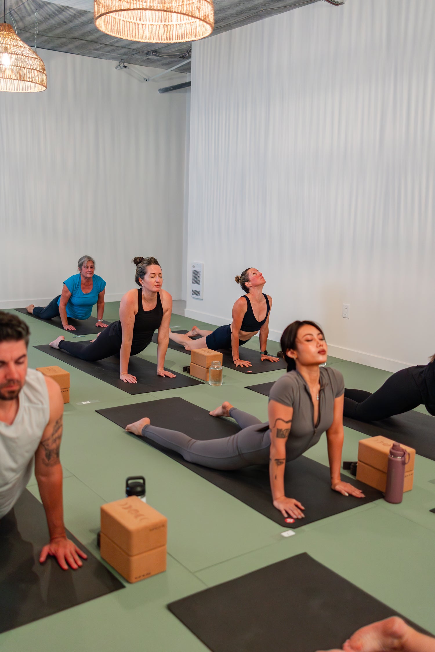 Diverse group of students of all ages and abilities practicing cobra pose at Prana Hot Yoga, demonstrating inclusive community where every body belongs
