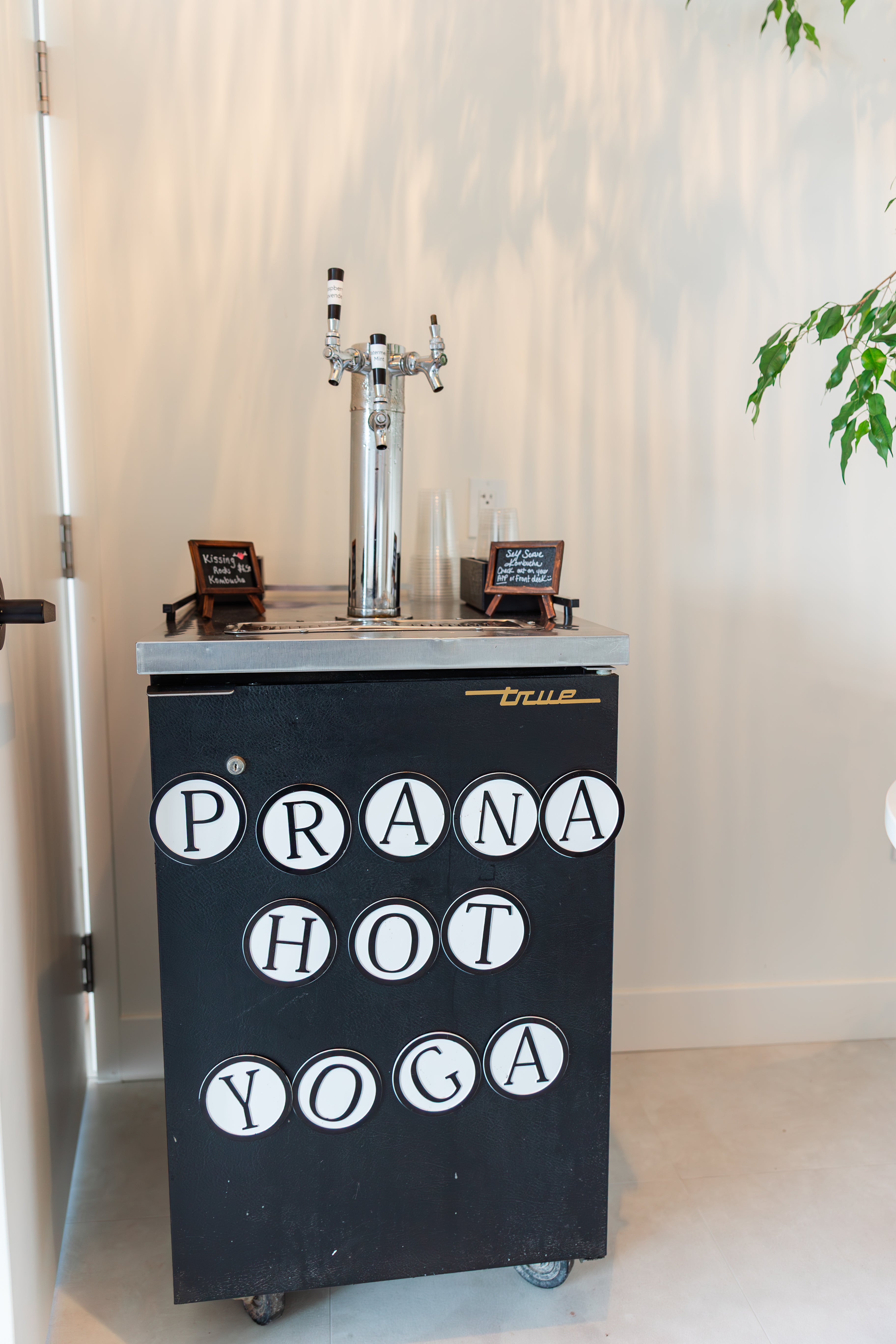 Prana Hot Yoga's hydration station featuring kombucha on tap, filtered water fountain, and complimentary glasses for members to stay refreshed during practice