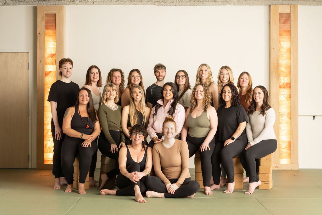 Prana Hot Yoga instructor team and staff gathered in studio, showing diverse group of certified yoga teachers ready to welcome students in Fredericton
