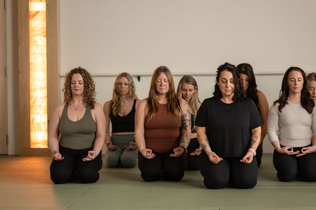 Students in meditation during hot yoga class at Prana Hot Yoga, demonstrating mindful practice and respect for sacred space with Himalayan salt panel glowing