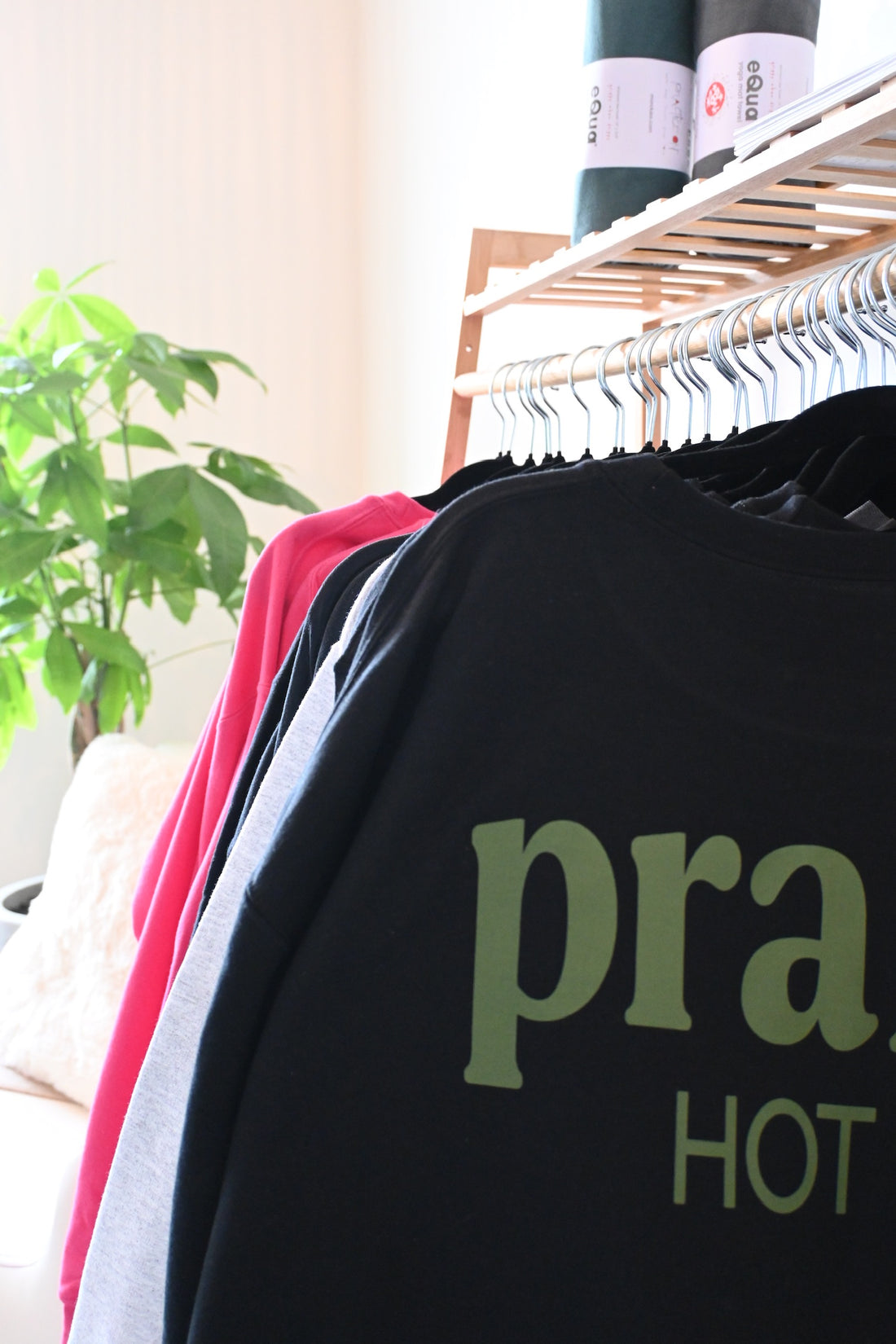 Prana Hot Yoga merchandise collection featuring branded tanks, tees, and apparel in eco-friendly fabrics displayed on boutique clothing rack