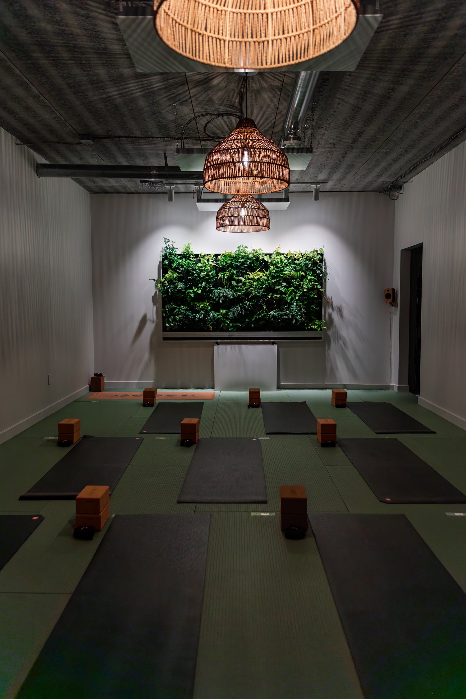 Prana Hot Yoga's Moon Room featuring unheated studio space with living botanical wall, ambient pendant lighting, and yoga mats with props set up for restorative practice"